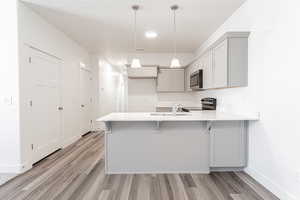 Kitchen featuring light hardwood / wood-style flooring, stainless steel appliances, decorative light fixtures, sink, and kitchen peninsula