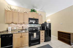 Kitchen with light tile patterned flooring, backsplash, sink, light brown cabinetry, and black appliances