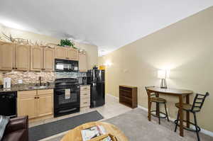 Kitchen with light brown cabinets, decorative backsplash, light tile patterned floors, sink, and black appliances