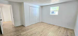 Unfurnished bedroom with light wood-type flooring, a closet, and a textured ceiling