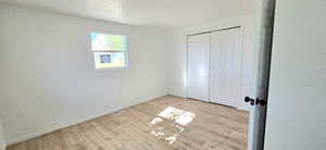 Unfurnished bedroom featuring a textured ceiling, light hardwood / wood-style flooring, and a closet