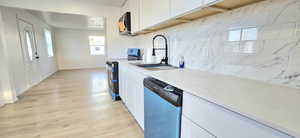 Kitchen featuring appliances with stainless steel finishes, light hardwood / wood-style flooring, white cabinetry, and backsplash