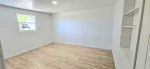 Unfurnished room with light wood-type flooring and a textured ceiling