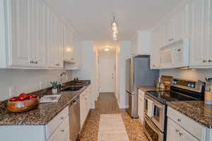 Kitchen featuring dark stone counters, appliances with stainless steel finishes, sink, and white cabinets