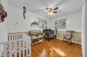 Bedroom with hardwood / wood-style floors, a nursery area, a textured ceiling, and ornamental molding