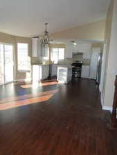 Kitchen with vaulted ceiling, appliances with stainless steel finishes, decorative light fixtures, white cabinetry, and dark wood-type flooring