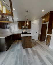 Kitchen featuring sink, stainless steel appliances, a kitchen island, decorative light fixtures, and light wood-type flooring