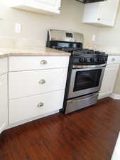 Kitchen with dark hardwood / wood-style flooring, gas stove, and white cabinets