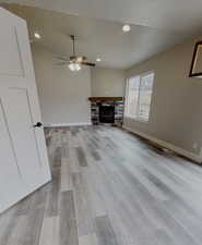 Unfurnished living room featuring ceiling fan, a stone fireplace, a textured ceiling, and light wood-type flooring
