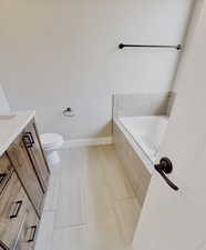 Bathroom featuring vanity, a relaxing tiled tub, tile patterned floors, and toilet
