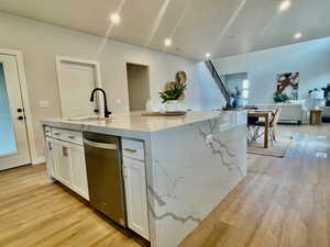 Kitchen with white cabinets, light stone counters, an island with sink, and light hardwood / wood-style flooring