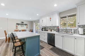 Kitchen with sink, light hardwood / wood-style floors, white cabinetry, and stainless steel dishwasher