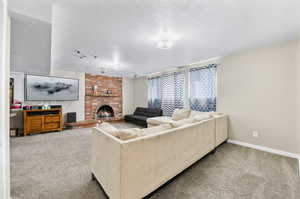 Carpeted living room with a fireplace, brick wall, and a textured ceiling