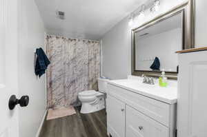 Bathroom featuring a shower with shower curtain, vanity, a textured ceiling, toilet, and hardwood / wood-style flooring