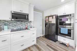 Kitchen featuring appliances with stainless steel finishes, light hardwood / wood-style floors, white cabinetry, and backsplash