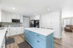 Kitchen featuring light hardwood / wood-style flooring, a kitchen island, tasteful backsplash, blue cabinetry, and appliances with stainless steel finishes