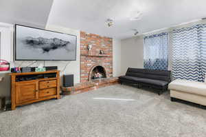 Carpeted living room featuring a textured ceiling, a brick fireplace, and brick wall