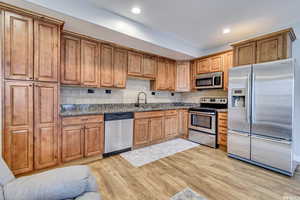 Basement Kitchen featuring appliances with stainless steel finishes, tasteful backsplash, sink, light wood-type flooring, and dark stone countertops