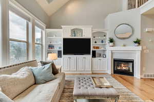 Living room with high ceiling, light hardwood  flooring, fireplace, and built in shelves