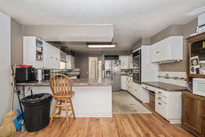 Kitchen featuring stainless steel appliances, hardwood flooring, backsplash, white cabinetry, and kitchen peninsula