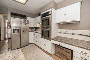 Kitchen with appliances with stainless steel finishes, white cabinetry, a textured ceiling, and backsplash. Subflooring.