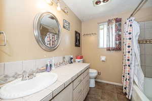 Full bathroom with shower / tub combo with curtain, vanity, tile patterned floors, a textured ceiling, and toilet