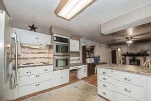 Kitchen with ceiling fan, light wood-type flooring, tasteful backsplash, white cabinetry, and stainless steel appliances. Subflooring.