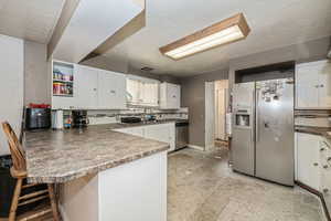 Kitchen with kitchen peninsula, stainless steel appliances, white cabinets, and backsplash. Subflooring.