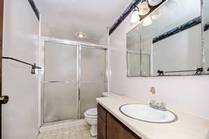 Bathroom featuring tile patterned flooring, a shower with door, vanity, and toilet