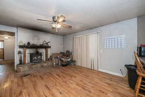 Living room with a fireplace, ceiling fan, a textured ceiling, and hardwood flooring