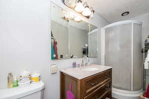 Bathroom with a shower with door, toilet, a textured ceiling, and vanity