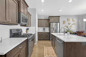 Kitchen with hard surface flooring, gas stove, backsplash, appliances with stainless steel finishes, sink, and a center island with sink