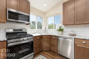 Kitchen featuring decorative backsplash, dark hardwood / wood-style flooring, vaulted ceiling, sink, and stainless steel appliances