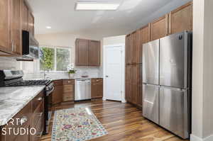 Kitchen featuring backsplash, dark wood-type flooring, vaulted ceiling, sink, and stainless steel appliances