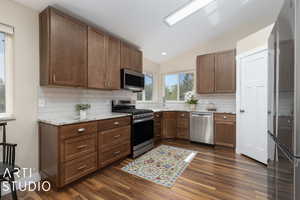 Kitchen with appliances with stainless steel finishes, dark wood-type flooring, and decorative backsplash