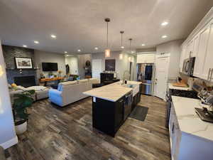 Kitchen with dark hardwood / wood-style floors, light stone countertops, a fireplace, a center island with sink, and stainless steel appliances