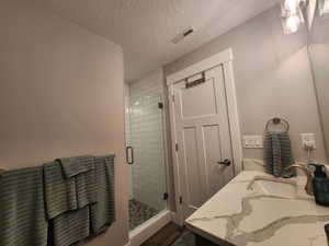 Bathroom with an enclosed shower, a textured ceiling, and vanity