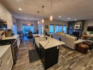 Kitchen featuring gas range, a fireplace, pendant lighting, a kitchen island with sink, and dark wood-type flooring