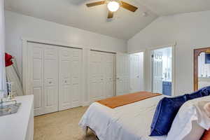 Carpeted bedroom featuring ceiling fan, ensuite bathroom, multiple closets, and lofted ceiling