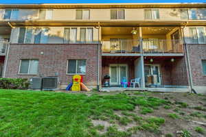 Rear view of property featuring a balcony, cooling unit, a patio area, and a lawn