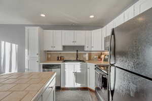 Kitchen with sink, tasteful backsplash, white cabinetry, and appliances with stainless steel finishes