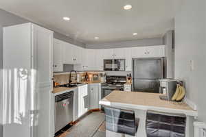 Kitchen with tile countertops, white cabinetry, and appliances with stainless steel finishes