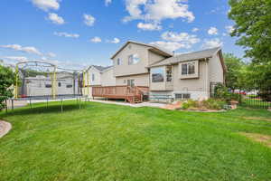 Rear view of property with a trampoline, a deck, and a yard