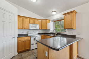 Kitchen featuring sink, kitchen peninsula, lofted ceiling, and white appliances