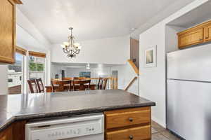 Kitchen with a notable chandelier, pendant lighting, white appliances, and light tile patterned floors