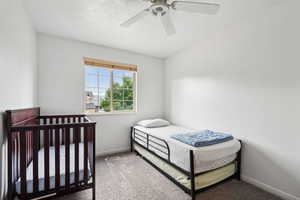 Bedroom with ceiling fan, carpet, and a nursery area