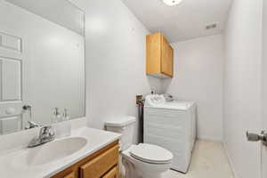 Bathroom with tile patterned floors, washing machine and clothes dryer, vanity, and toilet