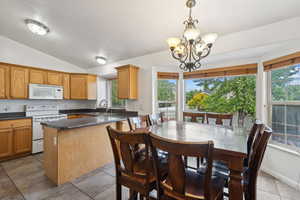 Kitchen with pendant lighting, tile patterned flooring, vaulted ceiling, sink, and white appliances