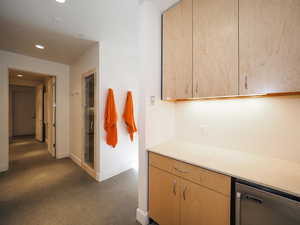 Kitchen with dishwasher, dark colored carpet, and light brown cabinetry