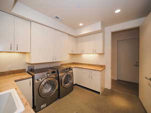 Washroom with sink, washing machine and dryer, and cabinets